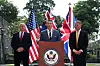 Pete Hegseth speaks at a podium as Richard Marles and John Healey stand beside U.S., Australian and British flags.