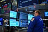 A trader in a blue jacket watches multiple financial screens on the NYSE trading floor.