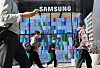 Pedestrians walk past the Samsung Gangnam storefront, with colorful digital panels behind them.